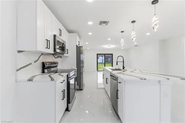 Kitchen featuring an island with sink, stainless steel appliances, white cabinetry, pendant lighting, and light stone countertops