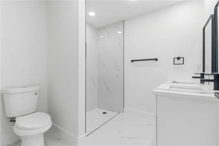 Bathroom with light marble finish flooring, double vanity, a marble finish shower, and recessed lighting