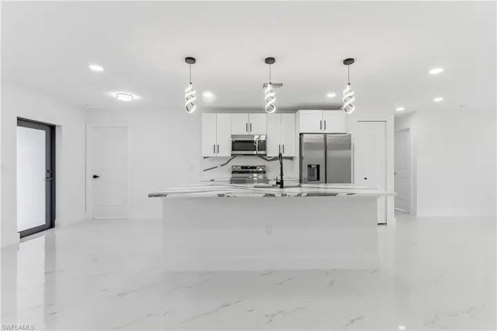 Kitchen featuring recessed lighting, stainless steel appliances, decorative light fixtures, white cabinetry, and a kitchen island with sink