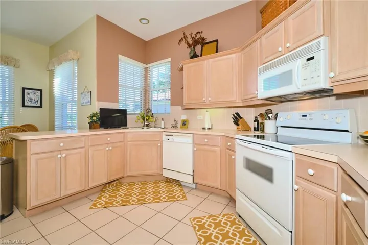 Kitchen with white appliances, light wood finish cabinets, light countertops, a peninsula, and light tile patterned floors