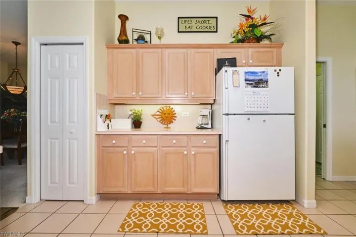 Kitchen with light countertops, freestanding refrigerator, light wood finish cabinetry, light tile patterned floors, and backsplash