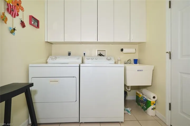 Laundry room featuring washing machine and dryer, light tile patterned floors, and cabinet space