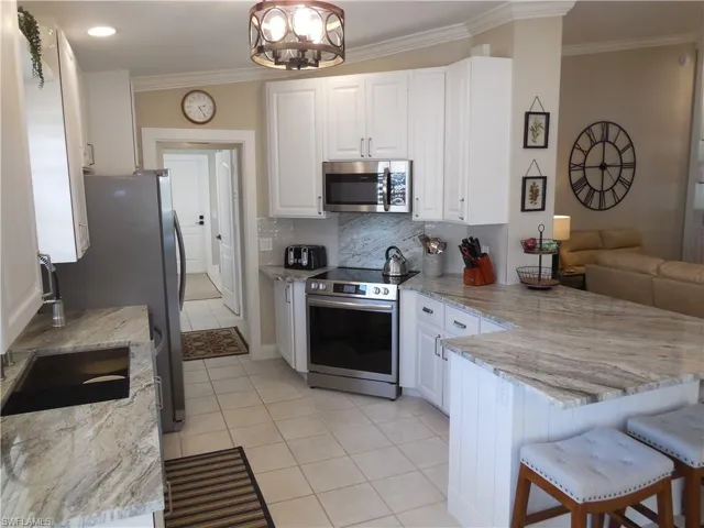 Kitchen featuring stainless steel appliances, light tile patterned flooring, crown molding, a peninsula, and white cabinetry