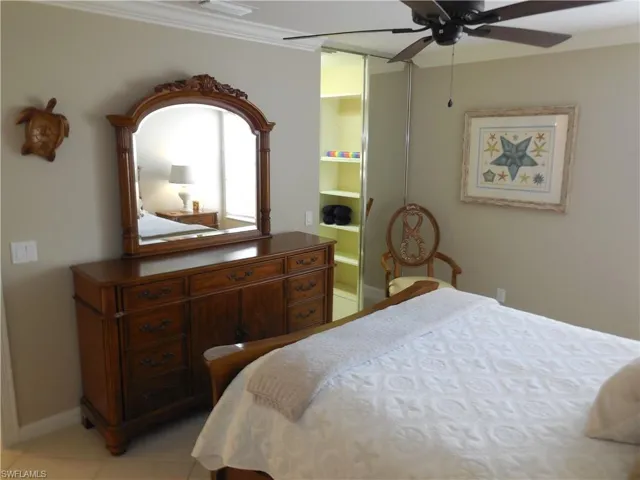 Bedroom featuring light tile patterned floors, ceiling fan, baseboards, ensuite bath, and ornamental molding