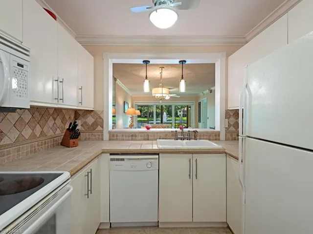 Kitchen featuring cream cabinets, sink, white appliances, tasteful backsplash, and lake view