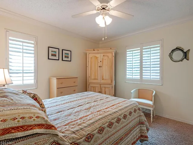 Carpeted bedroom with ceiling fan, multiple windows, and crown molding