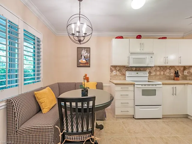Kitchen featuring cream appliances, tasteful backsplash, decorative light fixtures, an inviting chandelier, and light tile floors