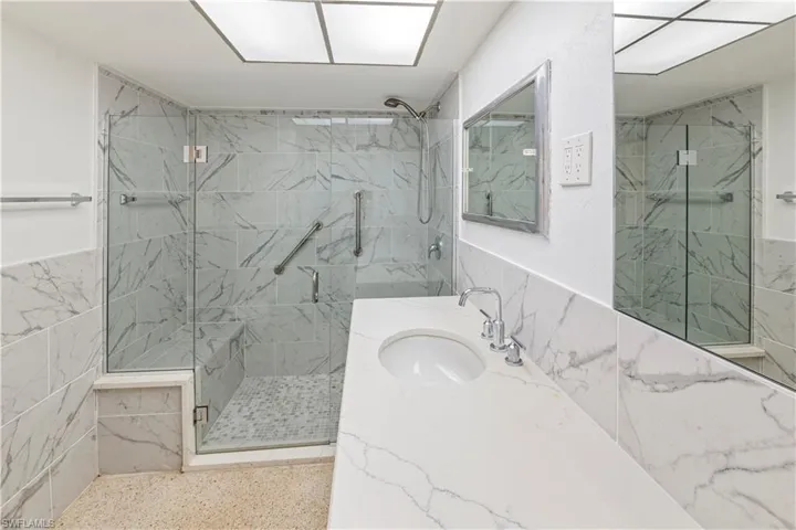 Bathroom featuring a glass-enclosed shower with a built-in bench, marble-type finish wall tiles, and a white countertop vanity with an integrated sink