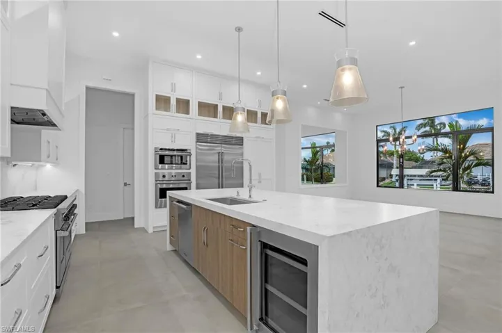 Kitchen featuring premium appliances, a kitchen island with sink, recessed lighting, light stone countertops, and glass insert cabinets