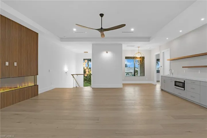 Unfurnished living room with light wood finished floors, a tray ceiling, a ceiling fan, recessed lighting, and a chandelier