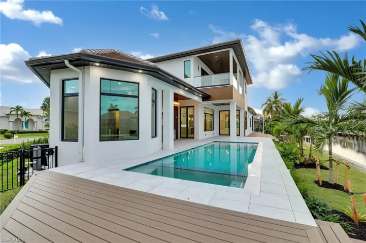 Rear view of house featuring a balcony, stucco siding, a patio area, and a pool with connected hot tub