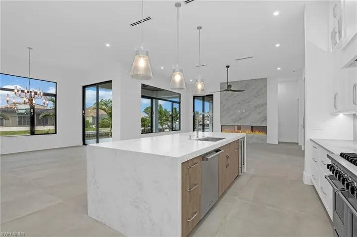 Kitchen with a chandelier, a large island, modern cabinets, appliances with stainless steel finishes, and light stone countertops