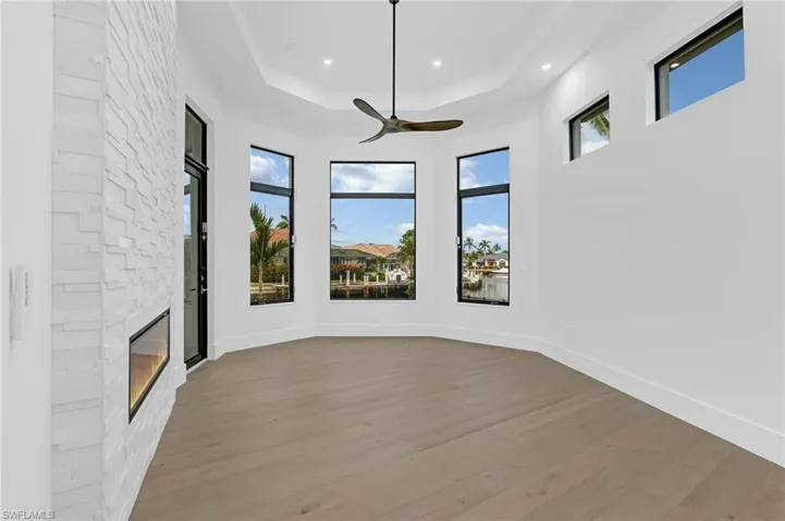 Unfurnished living room with wood finished floors, a ceiling fan, a raised ceiling, a fireplace, and recessed lighting