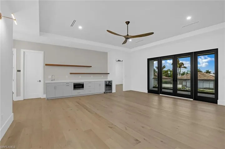 Unfurnished living room featuring light wood-style floors, a ceiling fan, a raised ceiling, recessed lighting, and beverage cooler