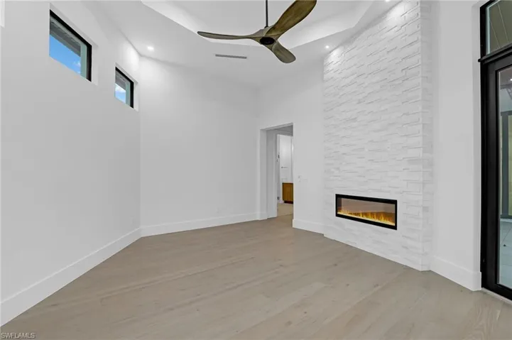 Unfurnished living room with a ceiling fan, light wood finished floors, a stone fireplace, a high ceiling, and recessed lighting