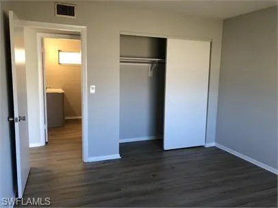 Unfurnished bedroom with dark wood-style floors, visible vents, a closet, and baseboards
