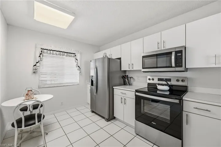 Kitchen featuring stainless steel appliances, light countertops, white cabinetry, light tile patterned flooring, and a textured ceiling
