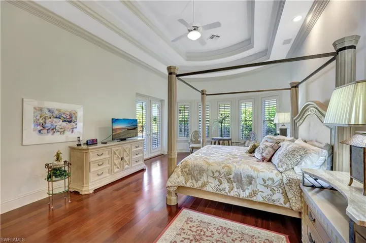 Bedroom featuring a tray ceiling, crown molding, dark wood-style flooring, and ceiling fan