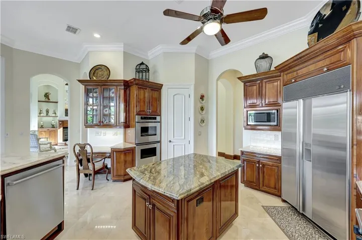 Kitchen featuring built in appliances, backsplash, glass insert cabinets, arched walkways, and light stone counters