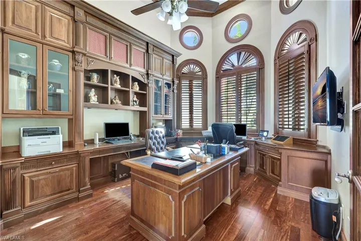 Office featuring a ceiling fan, dark wood-style floors, crown molding, a towering ceiling, and a wainscoted wall
