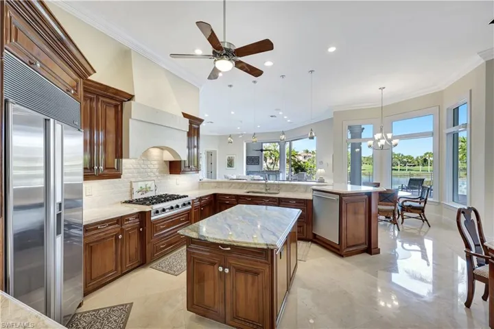 Kitchen featuring a peninsula, crown molding, stainless steel appliances, light stone countertops, and a center island