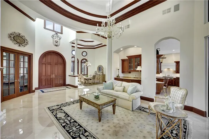 Living area featuring a high ceiling, crown molding, a chandelier, arched walkways, and french doors