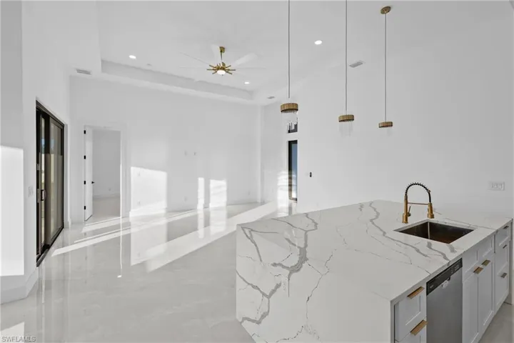 Kitchen featuring light stone countertops, stainless steel dishwasher, a raised ceiling, sink, and pendant lighting