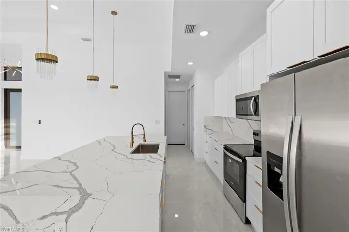 Kitchen featuring light stone countertops, appliances with stainless steel finishes, sink, white cabinetry, and hanging light fixtures