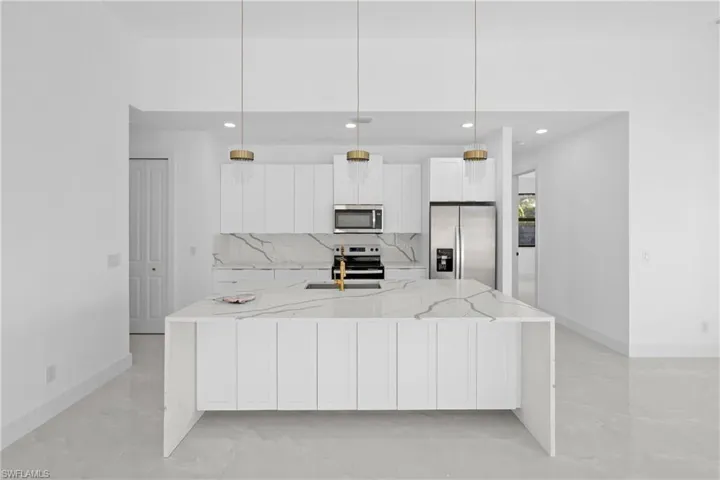 Kitchen with pendant lighting, white cabinetry, light stone countertops, and stainless steel appliances