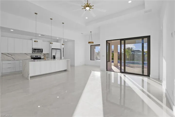 Kitchen with white cabinetry, a large island, a raised ceiling, pendant lighting, and appliances with stainless steel finishes