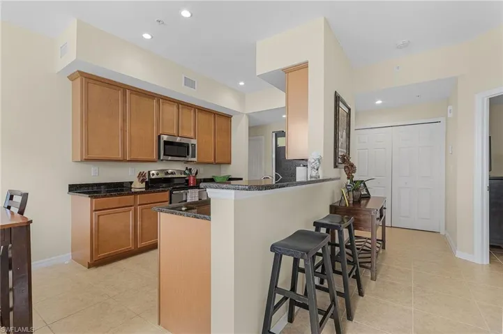 Kitchen with dark stone countertops, light tile patterned floors, stainless steel appliances, kitchen peninsula, and a breakfast bar area