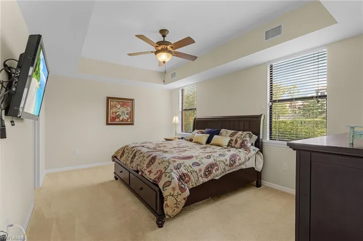 Bedroom with a raised ceiling, ceiling fan, and light carpet