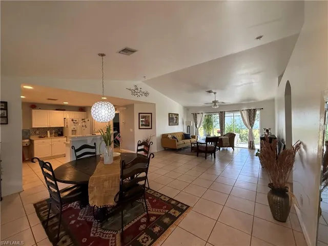 Dining area featuring lofted ceiling, light tile patterned floors, arched walkways, and a ceiling fan