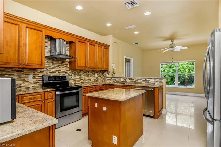Kitchen featuring backsplash, wall chimney range hood, light tile patterned floors, and a center island