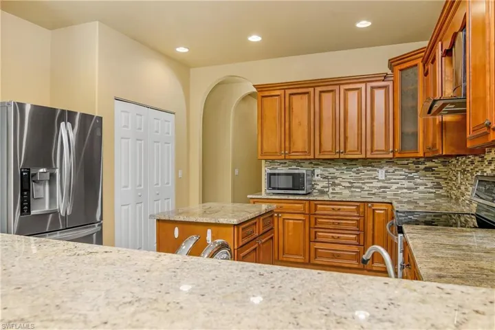 Kitchen with appliances with stainless steel finishes, backsplash, wall chimney range hood, and light stone countertops