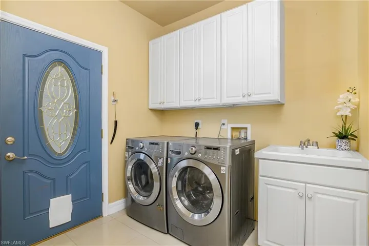 Laundry area featuring light tile patterned flooring, sink, cabinets, and washer and dryer