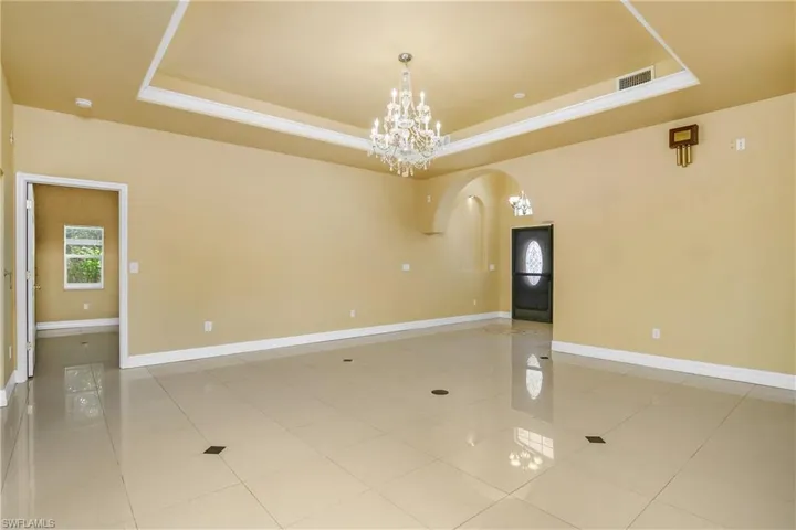 Empty room with a raised ceiling, a chandelier, and light tile patterned floors