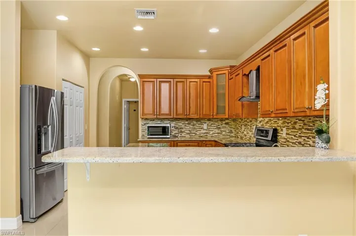 Kitchen with appliances with stainless steel finishes, light stone countertops, tasteful backsplash, kitchen peninsula, and wall chimney range hood