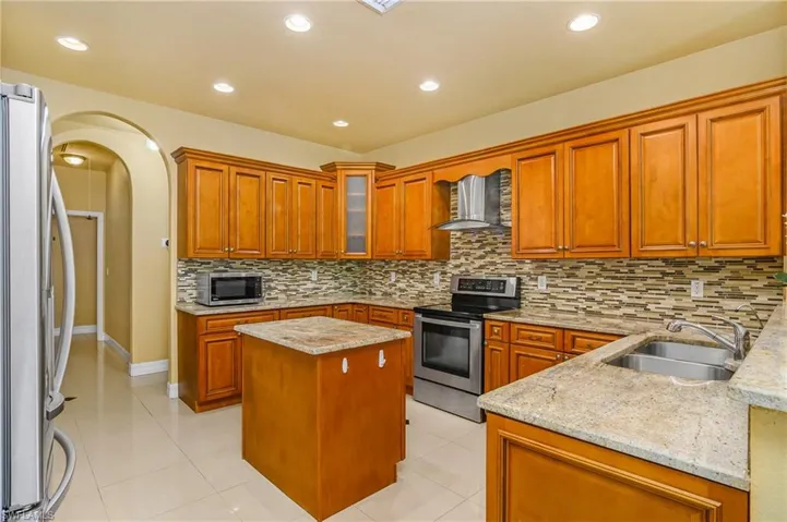 Kitchen with appliances with stainless steel finishes, backsplash, sink, a center island, and wall chimney range hood