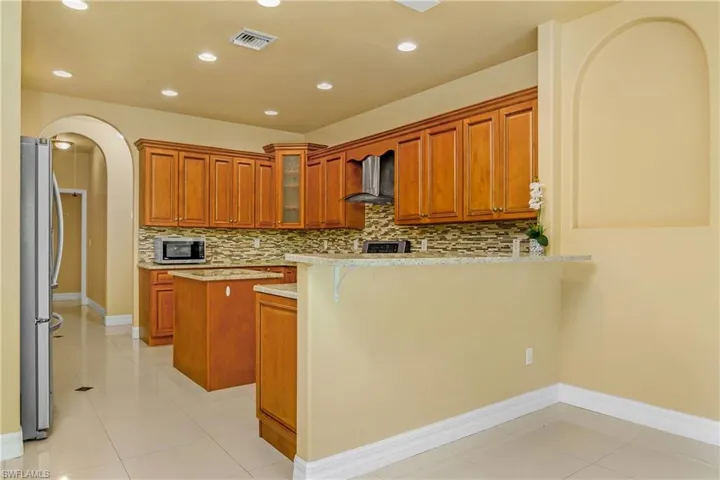 Kitchen with light tile patterned flooring, wall chimney range hood, stainless steel appliances, and backsplash
