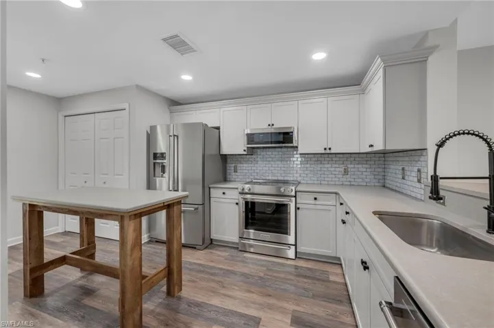 Kitchen featuring stainless steel appliances, white cabinets, light wood-type flooring, light stone counters, and decorative backsplash