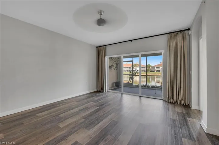 Unfurnished room with a water view, dark wood finished floors, and a ceiling fan