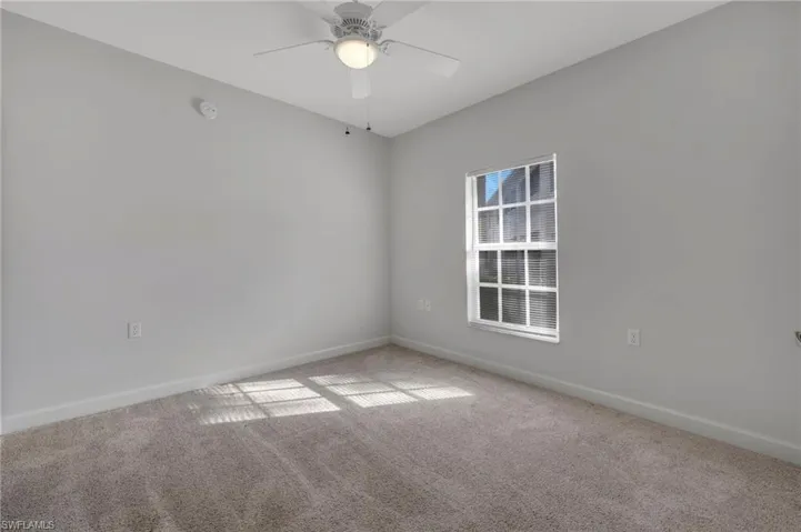 Carpeted empty room featuring baseboards and a ceiling fan