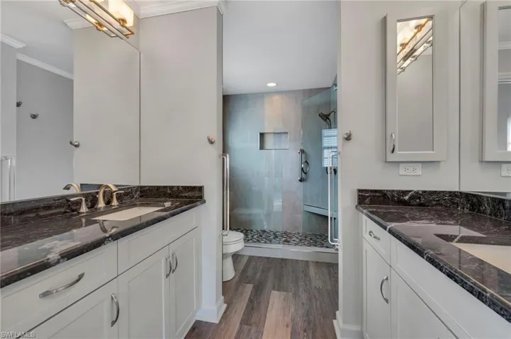 Bathroom featuring two vanities, a shower stall, dark wood-style flooring, crown molding, and recessed lighting