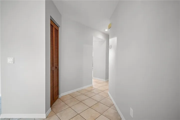 Hallway featuring diagonal tile flooring, white baseboards, light gray wall paint, and a louvered bifold door
