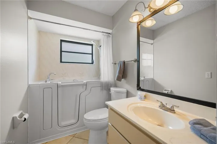 Bathroom featuring a walk-in tub with a shower attachment, a single vanity with an integrated sink, a large mirror, and tiled flooring