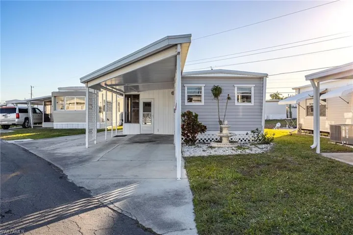 Manufactured / mobile home with driveway, a carport, central AC unit, and a front lawn