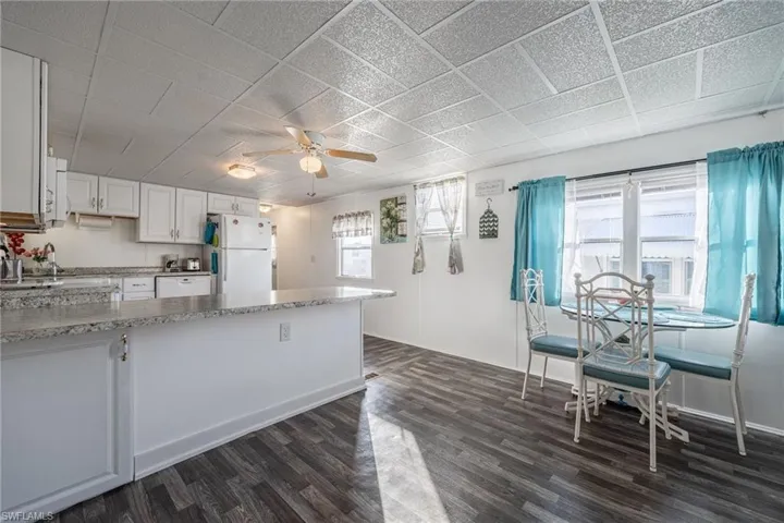 Kitchen with white appliances, a peninsula, dark wood-style flooring, and white cabinetry