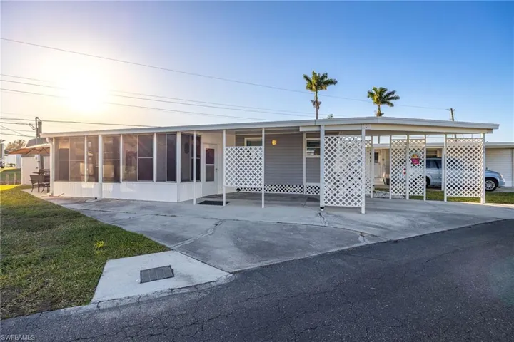 View of front facade featuring an attached carport, concrete driveway, a front lawn, and a sunroom