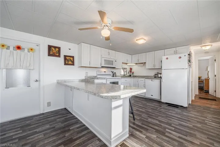 Kitchen with white appliances, white cabinets, a peninsula, and dark wood-type flooring